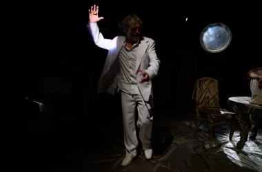 Zaciemniona sala, aktor w białym garniturze