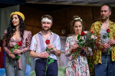 czterech aktorów stoją przed widownią z czerwonymi różami w ręce, po prawej wysoki mężczyzna w żółtej letniej koszulce obok niego