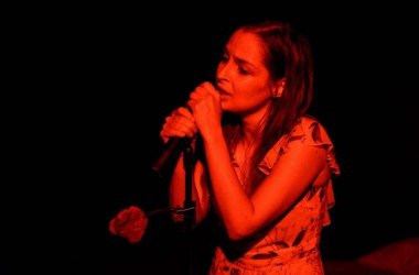 Zdjęcie aktorki, trzyma w rękach mikrofon, śpiewa, jest oświetlona czerwonym światłem