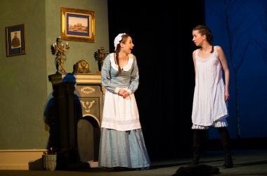 pokój, na środku młoda kobieta w niebieskiej sukience służąca śmieje sie do młodej kobiety w białej sukience z czarnymi warkoczykami