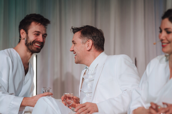 Zdjęcie dwóch mężczyzn i kobieta ubrani na biało, trzymają w ręce szklanki, uśmiechają się do siebie