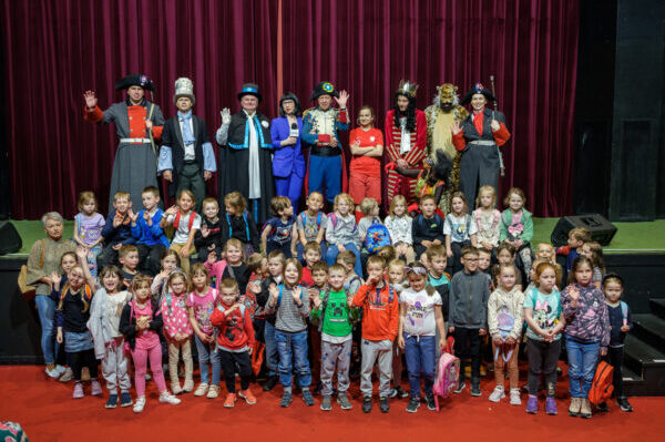 na scenie około czterdzieścioro dzieci śmieją się machają za nimi dziewięciu aktorów przebrani w kolorowe bajkowe kostiumy