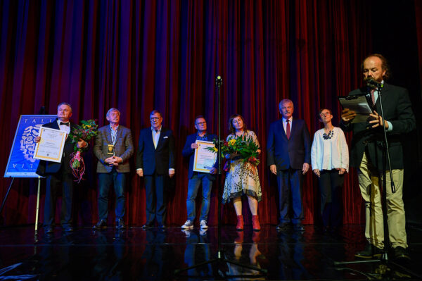 gala ogłoszenia nagród festiwalu komedii talia po prawej dyrektor teatru odczytuje nagrody z tyłu za nim dwie panie i czterech mężczyzn ubrani elegancko stoją z dyplomami